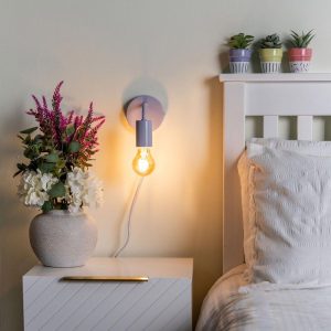 Plug in wall light in lilac, shown lit on bedroom wall