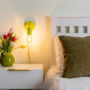 Plug in wall light in lime green, shown lit on bedroom wall