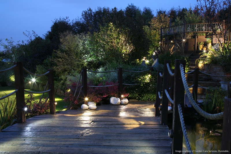 Illuminated garden scene with decking, lawns and shrubs at dusk