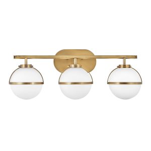 Hinkley Hollis 3 light bathroom mirror light in heritage brass with opal glass shades on white background.