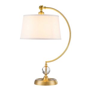 Quoizel Jenkins brushed brass table lamp with cream shade on white background, lit